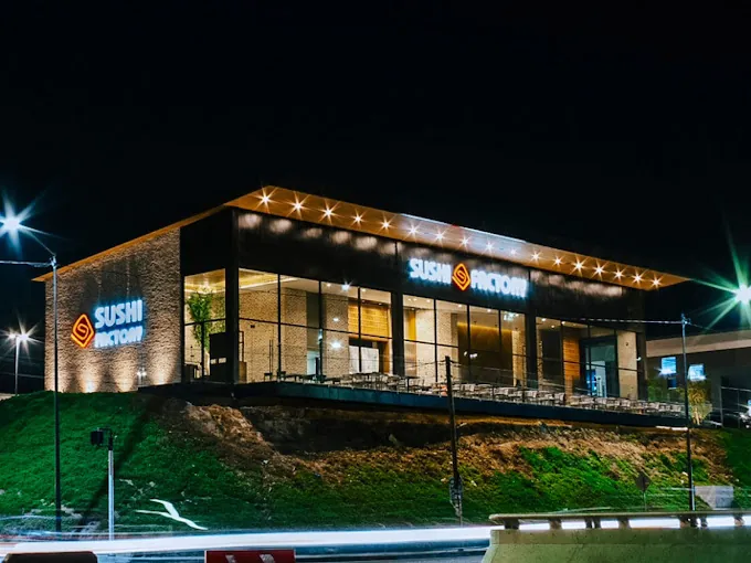 Restaurante Sushi Factory de noche con fachada de cristal iluminada